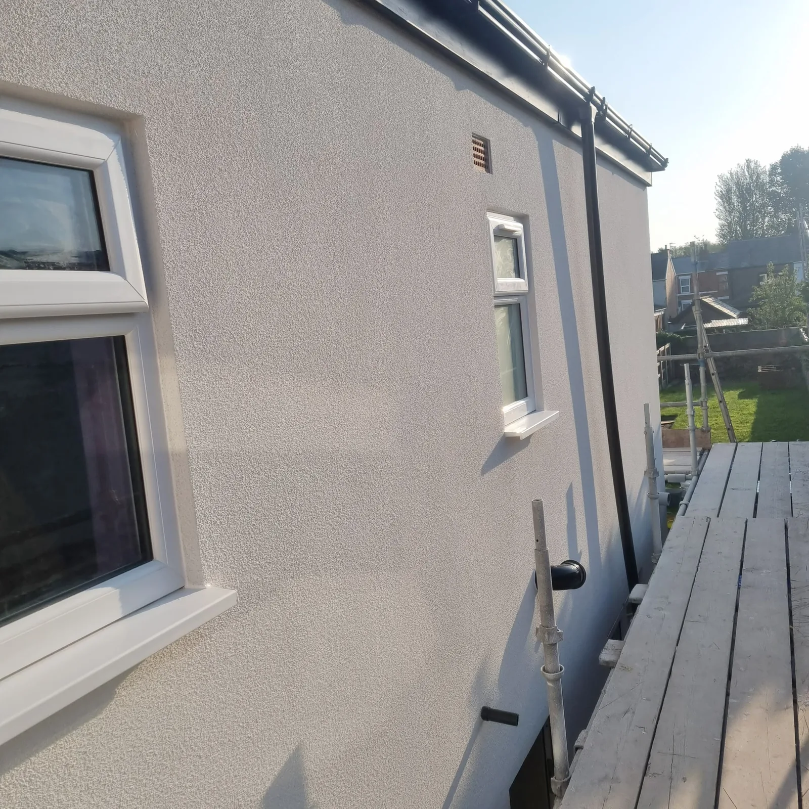 Textured silicone render catching low sun on a Southport side elevation